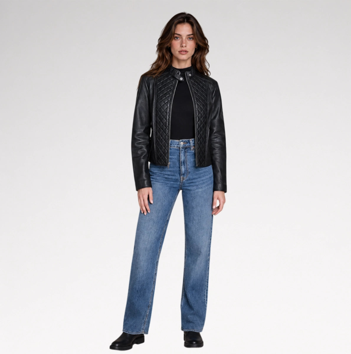 A women is wearing black quilted leather jacket in a grey background with a full pose. 