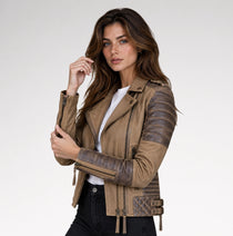 A woman modeling a brown faux-leather moto jacket with contrasting dark brown ribbed sleeves and a quilted detail on the lower front, worn over a white t-shirt and black jeans against a light gray studio background.