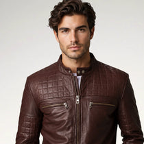 A man wearing a dark brown quilted leather jacket with silver zippers, photographed against a light gray studio background.