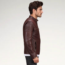 A man in profile wearing a dark brown leather jacket with quilted sleeve panels and a zippered chest pocket, photographed against a plain light gray studio background.