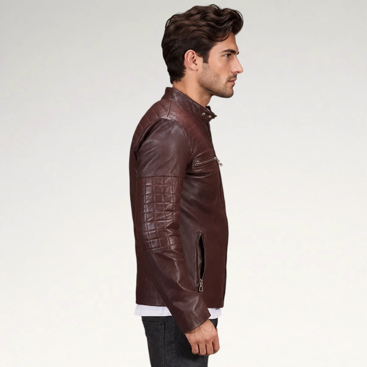 A man in profile wearing a dark brown leather jacket with quilted sleeve panels and a zippered chest pocket, photographed against a plain light gray studio background.