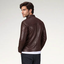 A man wearing a dark brown leather jacket with quilted shoulder panels, shown from a three-quarters back view against a light gray studio background.