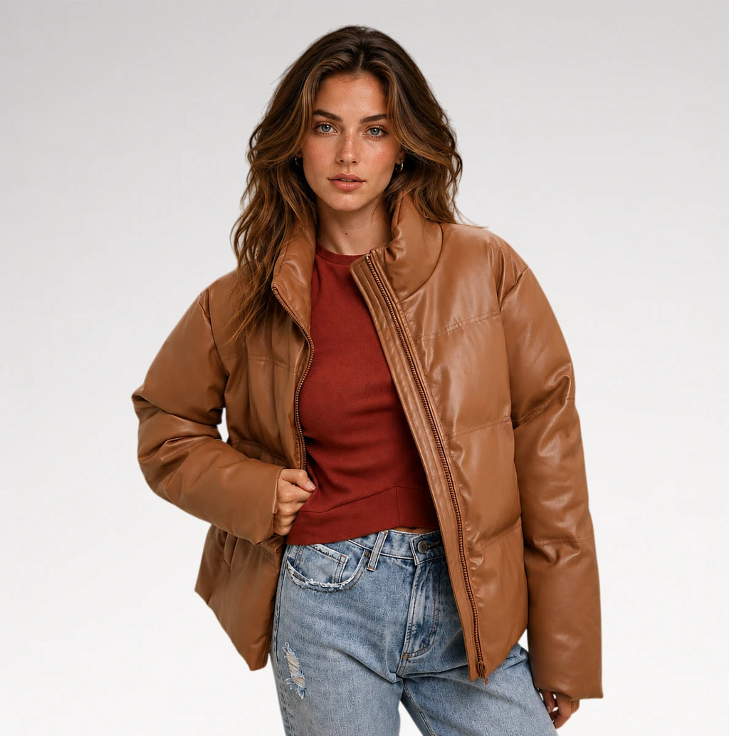 A woman modeling a brown faux-leather puffer jacket over a rust-red top and light-wash blue jeans, photographed against a clean light gray studio background.