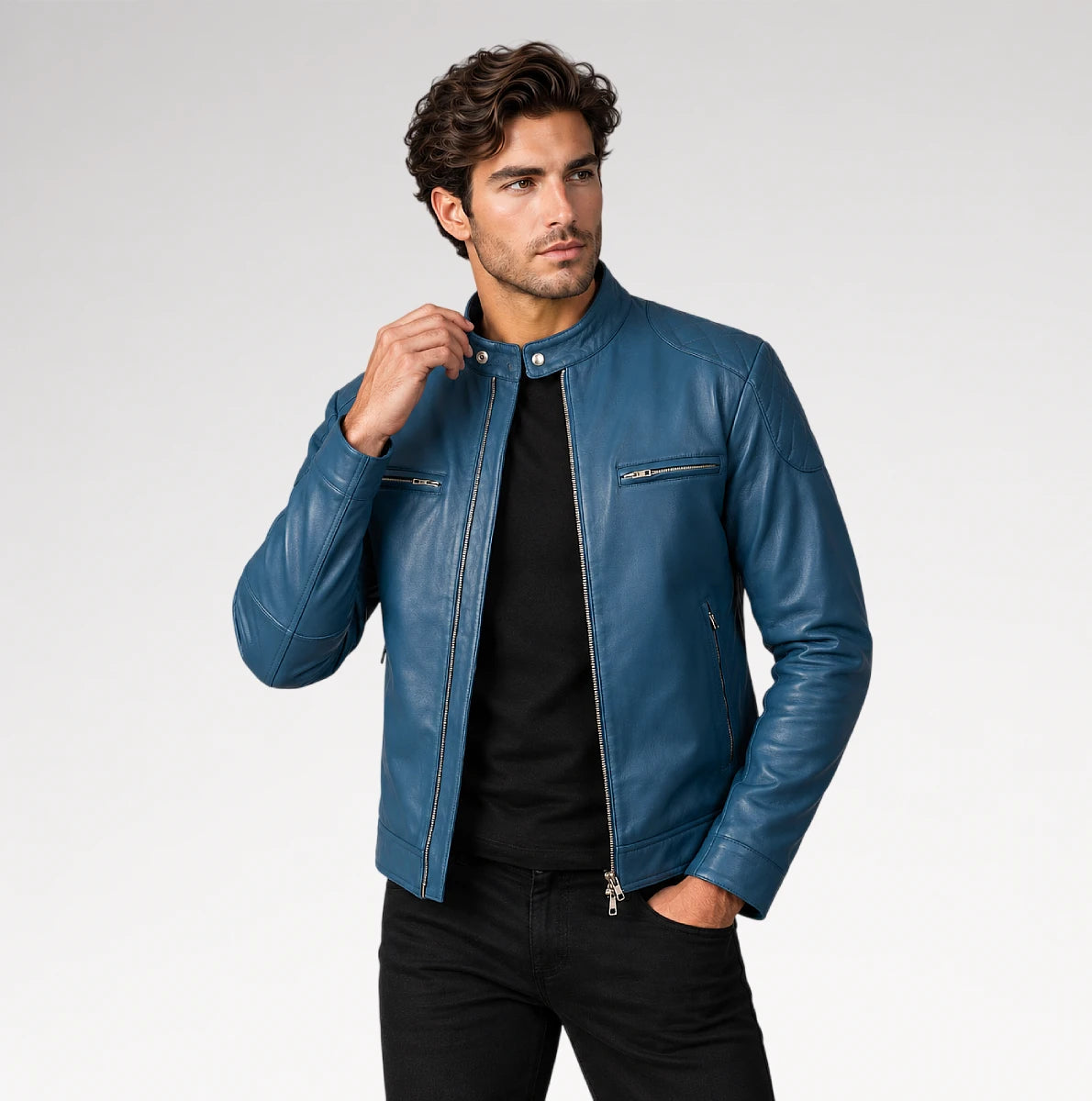 A man wearing a blue leather jacket over a black shirt and black pants, standing against a light gray studio background.
