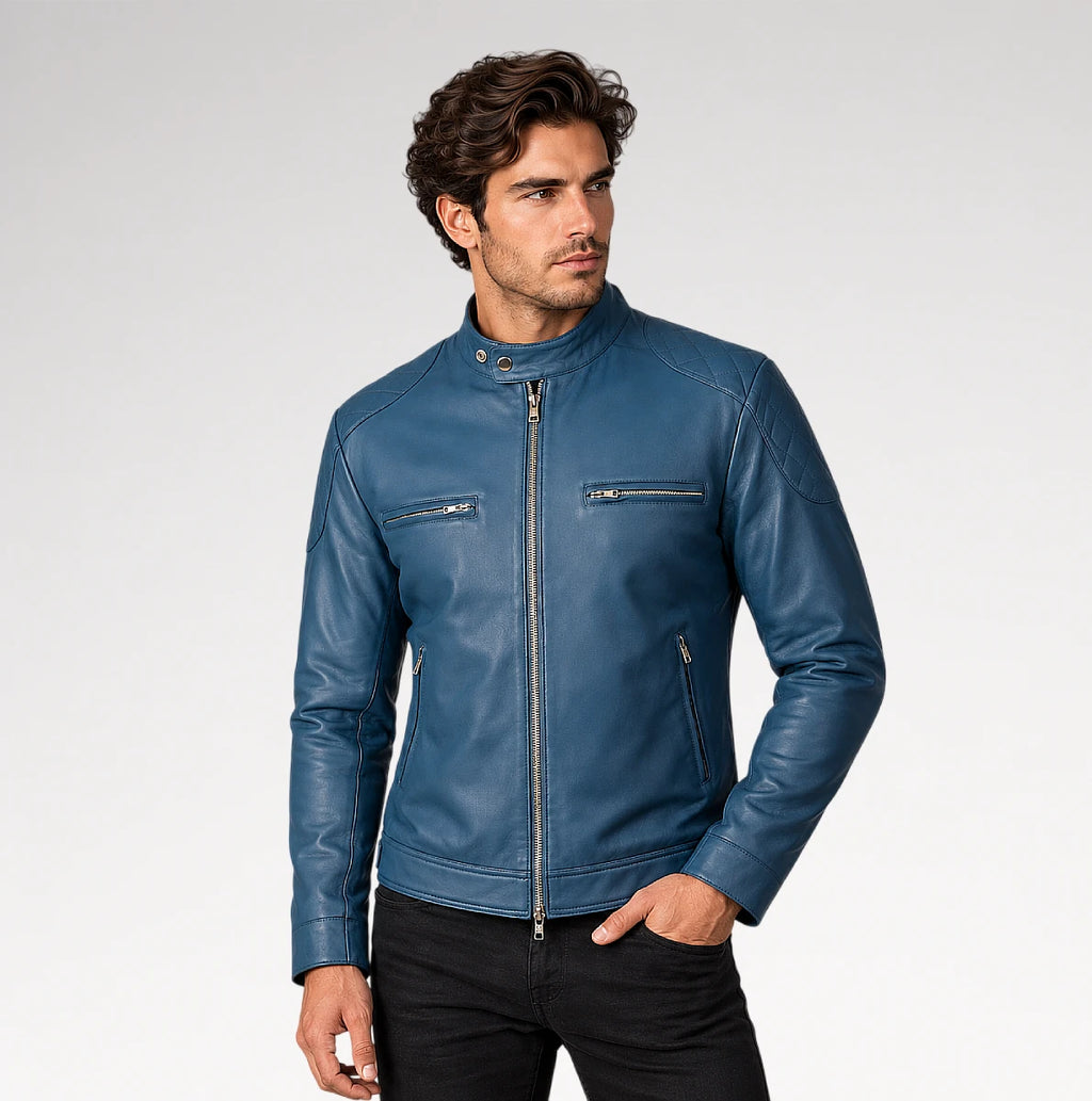A man wearing a blue leather motorcycle jacket with a stand collar, front zipper, and zippered chest pockets, paired with black pants, photographed against a light gray studio background.
