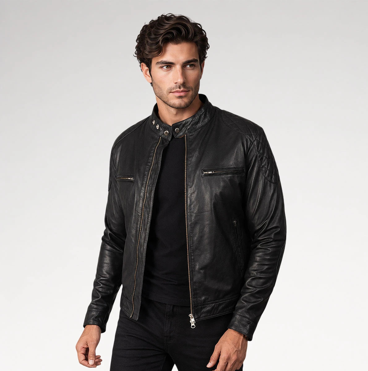 A man wearing a black leather biker jacket over a black t-shirt and black pants, standing against a light gray studio background. Main image