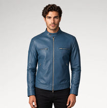 A man wearing a blue leather motorcycle jacket with a stand collar, front zipper, and zippered chest pockets, photographed against a light gray studio background.
