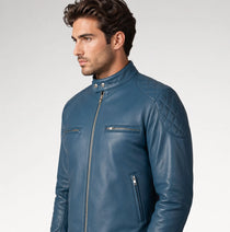A man wearing a blue leather motorcycle jacket with quilted shoulder panels and zippered pockets, photographed against a light gray studio background.