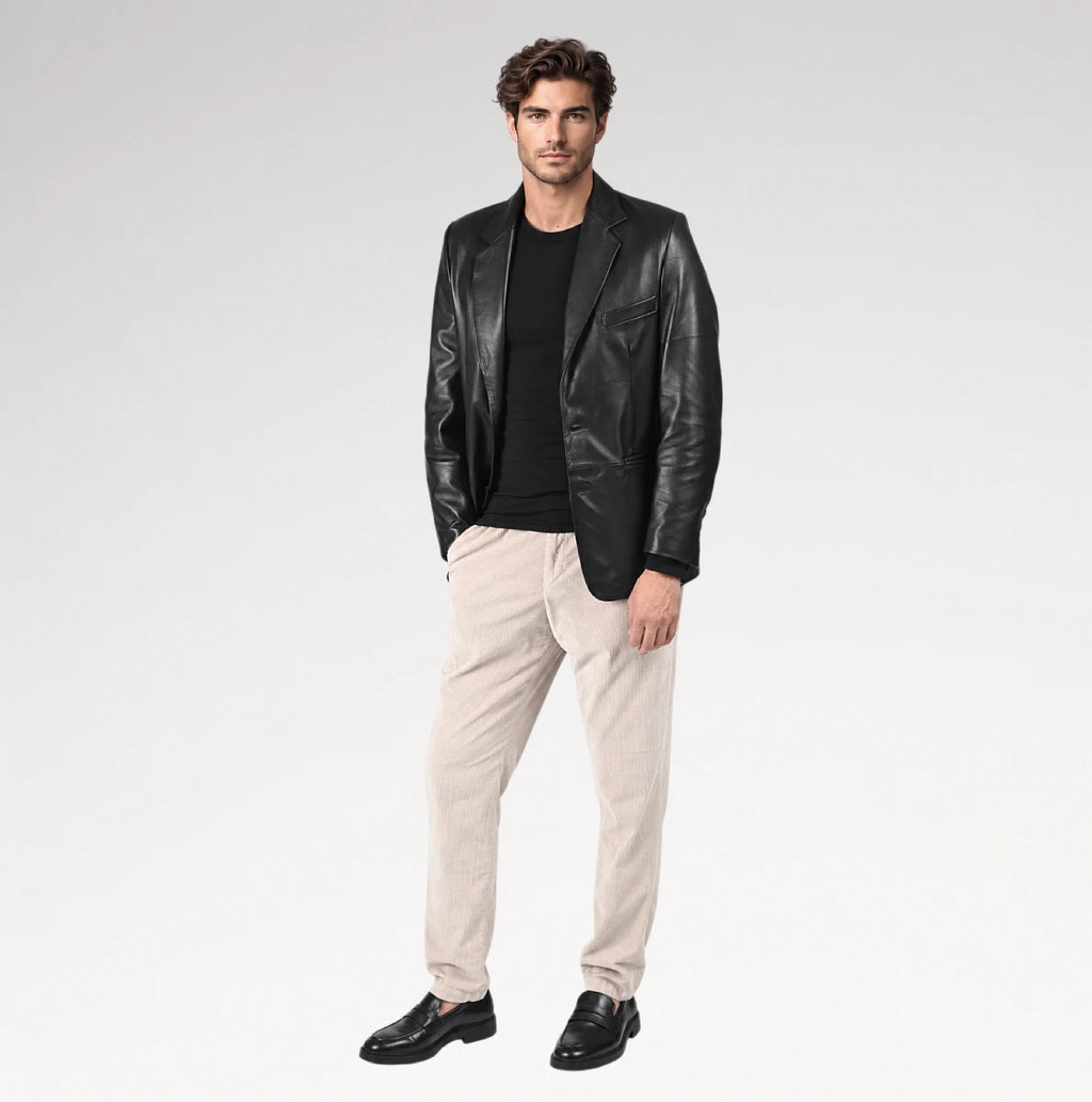 A man modeling a black leather blazer over a black t-shirt, paired with beige trousers and black leather loafers, against a light gray studio background.
