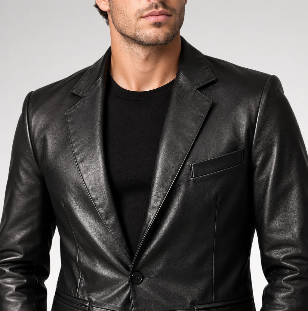 A man wearing a black leather blazer over a black crewneck t-shirt, shown from the chin down against a neutral gray studio background.