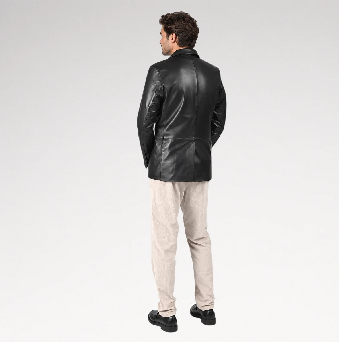 A man wearing a black leather blazer, beige trousers, and black shoes, shown from the back against a light gray studio background.