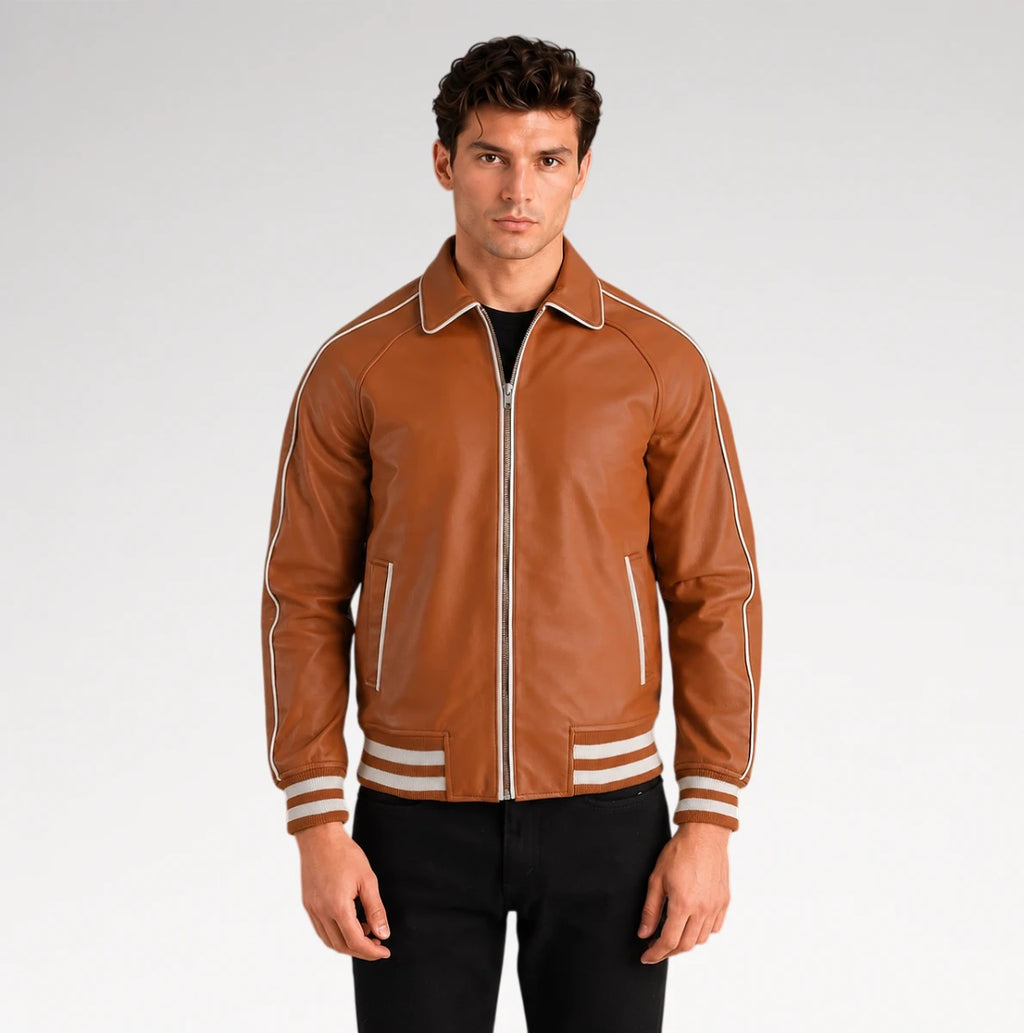 A man wearing a brown leather varsity-style jacket with white contrast piping and striped ribbed cuffs, paired with black pants, against a light gray studio background.