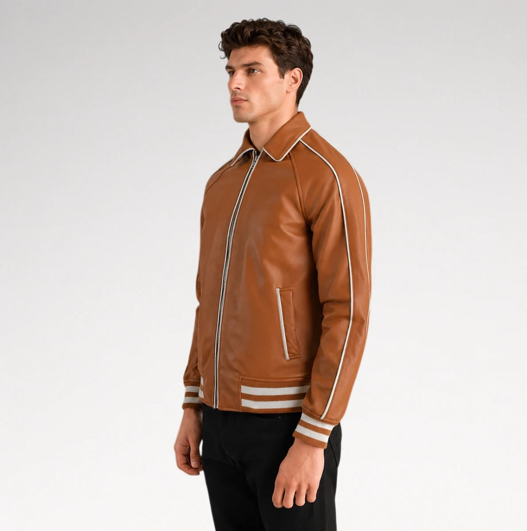 A man wearing a brown leather varsity-style jacket with white stripe details on the shoulders, sleeves, and cuffs, paired with black pants, photographed against a light gray studio background.