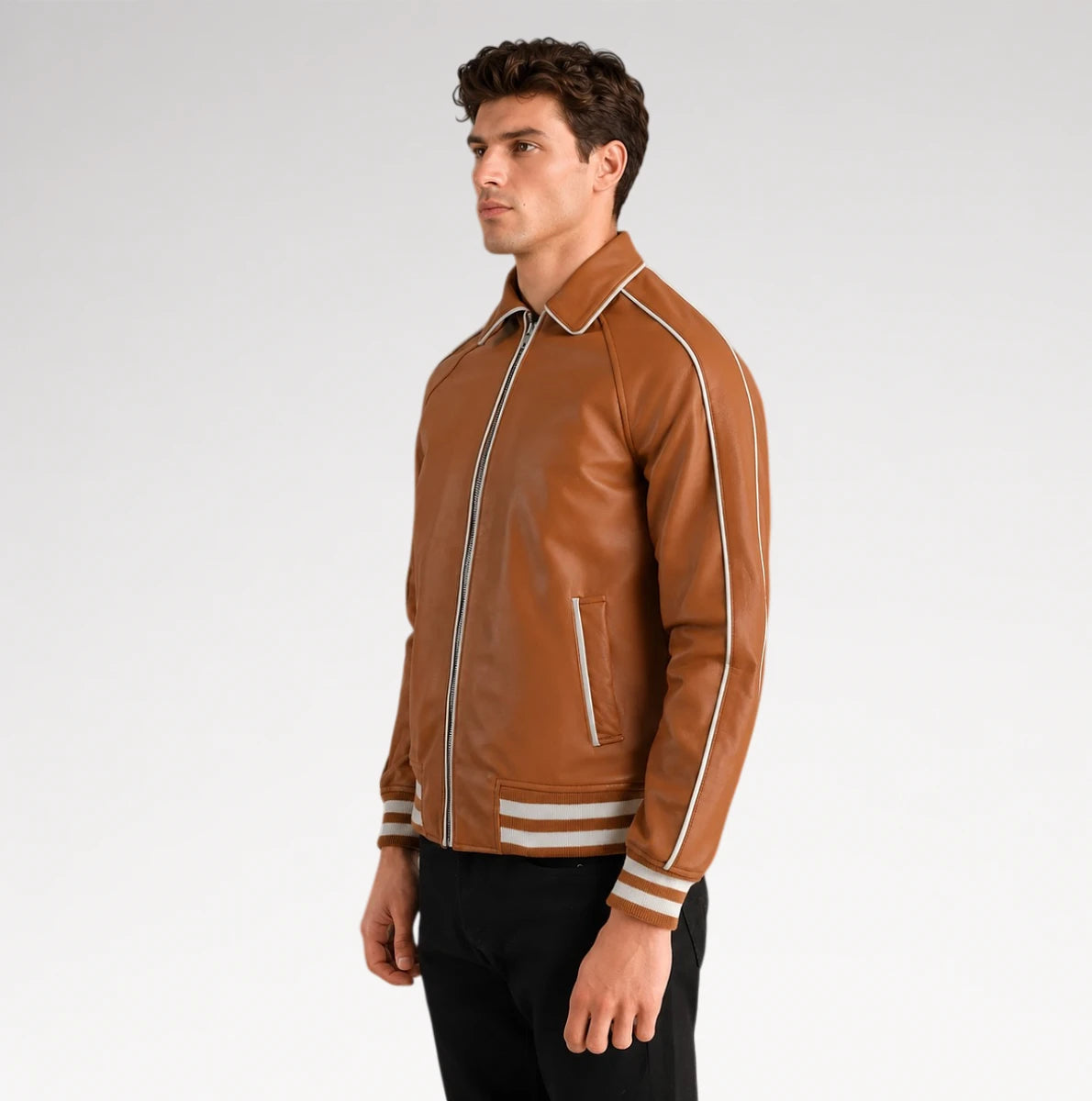 A man wearing a brown leather varsity-style jacket with white stripe details on the shoulders, sleeves, and cuffs, paired with black pants, photographed against a light gray studio background.