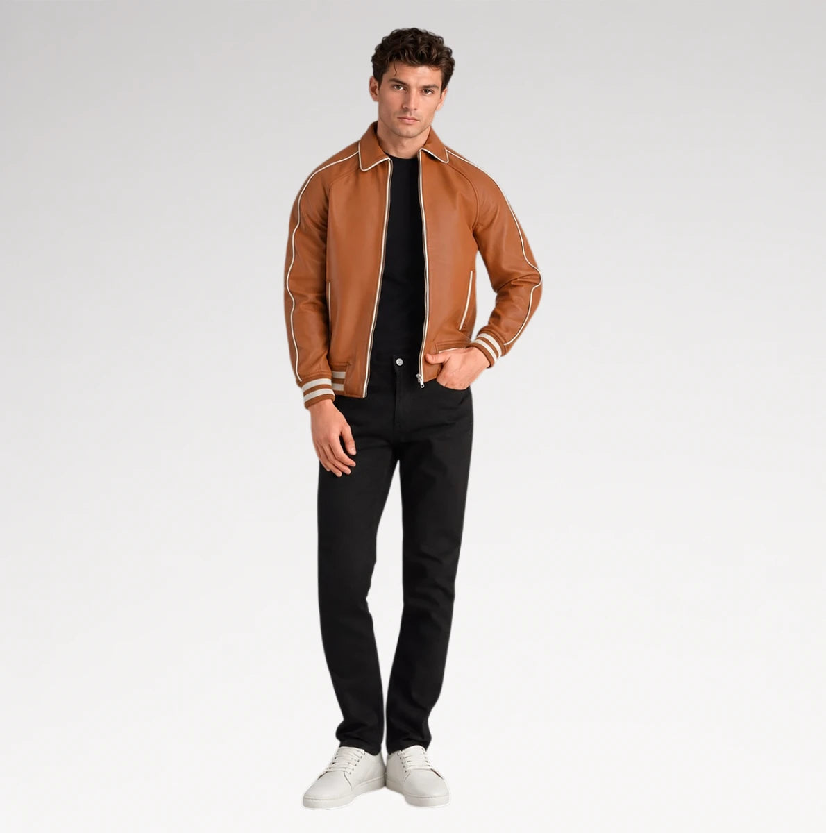 A man modeling a brown leather bomber jacket with cream stripes on the shoulders and cuffs, paired with a black t-shirt, black pants, and white sneakers, against a light gray studio background.