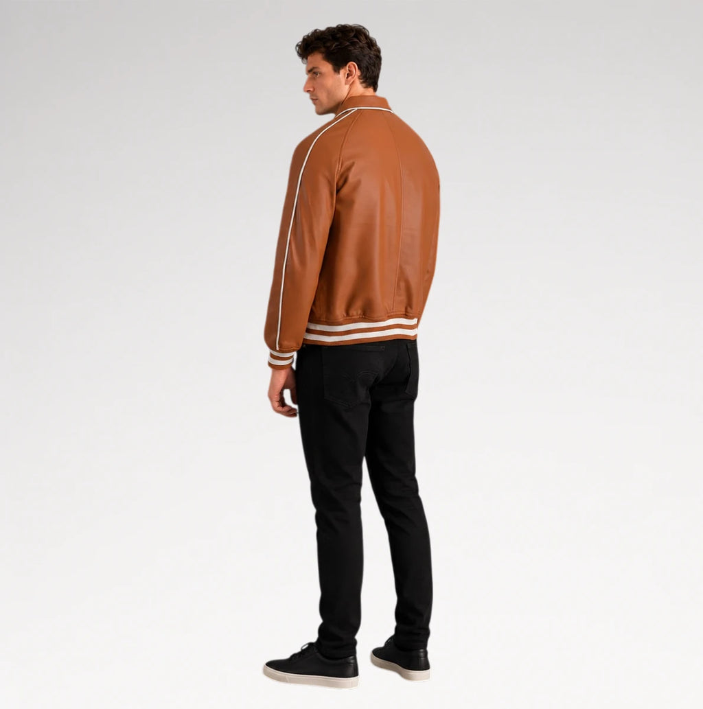 A man wearing a brown leather varsity-style jacket with white stripes on the shoulders and hem, paired with black pants and black sneakers, shown from a rear three-quarter view against a light gray studio background.