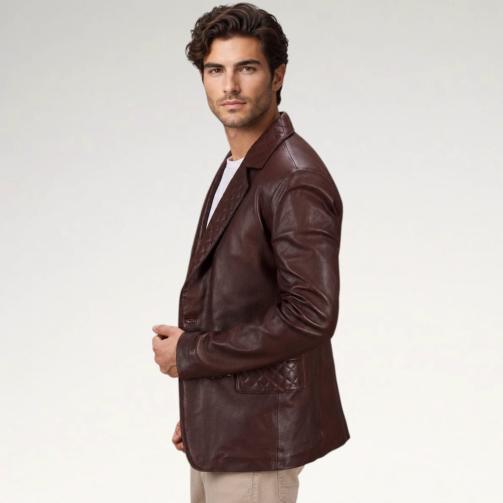 A man wearing a dark brown leather blazer with a quilted pocket detail, styled over a white t-shirt and beige pants, photographed against a light gray studio background.