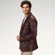 A man wearing a dark brown leather blazer with a quilted pocket detail, styled over a white t-shirt and beige pants, photographed against a light gray studio background.