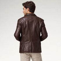 A man viewed from the back wearing a dark brown leather blazer with a quilted collar and beige trousers, set against a plain light gray studio background.