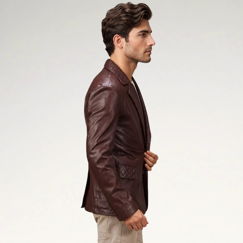 A man in profile wearing a dark brown leather blazer with quilted details on the chest and waist, paired with beige trousers, against a plain light gray studio background.