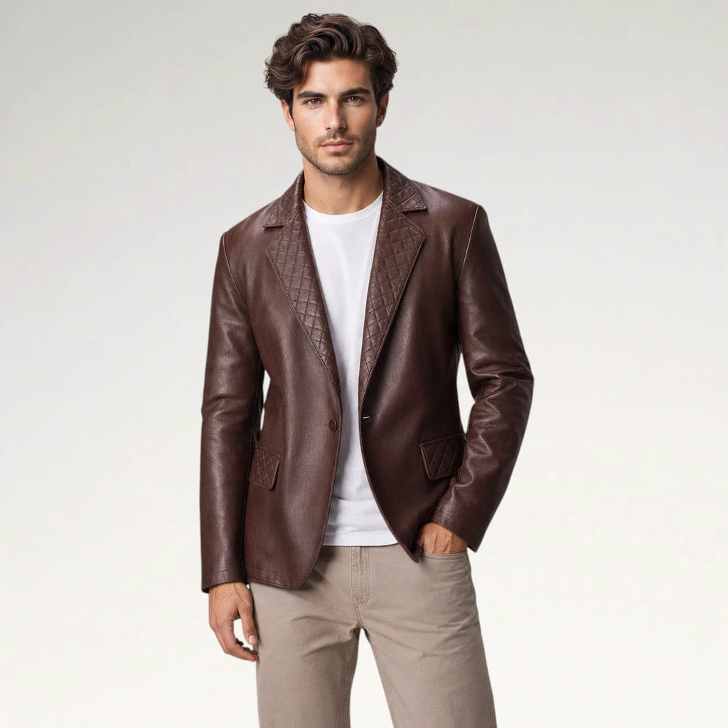 A man wearing a dark brown leather blazer with textured quilted lapels, styled over a white t-shirt and beige trousers, photographed against a light gray studio background.