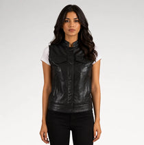A woman modeling a black faux-leather vest with a stand-up collar and front flap pockets, worn over a white t-shirt and black pants, against a light gray studio background.
