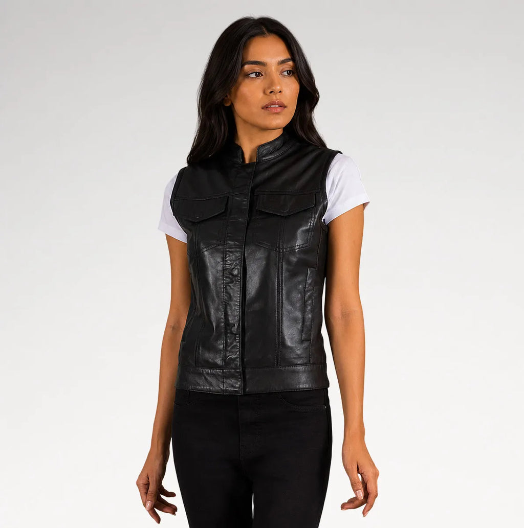 A woman modeling a black leather motorcycle vest over a white t-shirt and black pants, photographed against a neutral light gray studio background.
