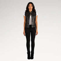 A woman modeling a black leather sleeveless vest over a white t-shirt and black skinny jeans, standing against a light gray studio background.