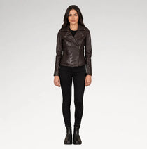 A woman modeling a dark brown leather moto jacket, paired with black skinny jeans and black ankle boots, against a light gray studio background.