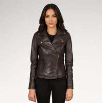 A woman modeling a dark brown faux-leather moto jacket with an asymmetrical zipper, set against a plain light gray studio background.