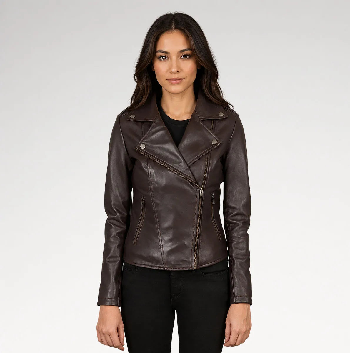 A woman modeling a dark brown faux-leather moto jacket with an asymmetrical zipper, set against a plain light gray studio background.