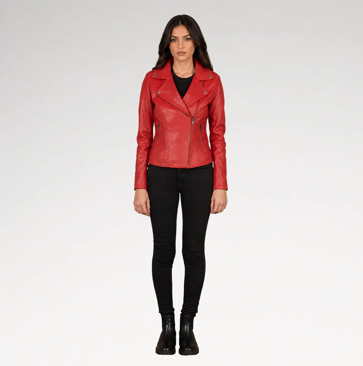 A woman modeling a red leather moto jacket over a black top and black skinny pants, standing against a light gray studio background.