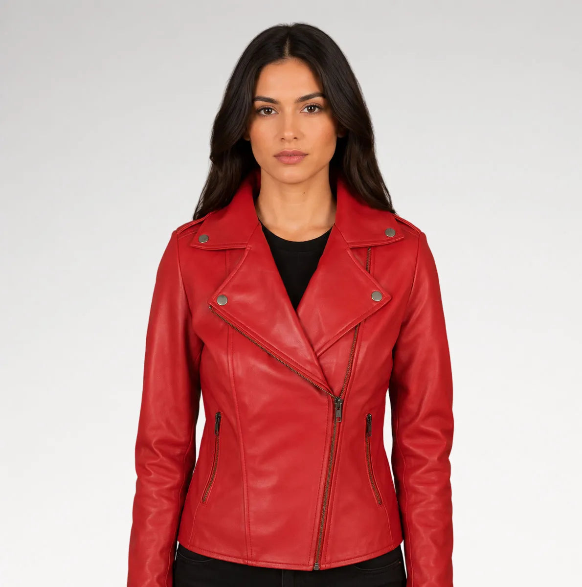 A woman modeling a bright red faux leather moto jacket with an asymmetrical zipper, set against a plain light gray studio background.