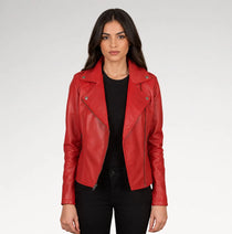 A woman modeling a bright red leather moto jacket over a black top and black pants, photographed against a light gray studio background.
