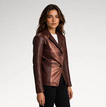 A woman modeling a metallic bronze-brown leather blazer with black pants, photographed against a clean light gray studio background.