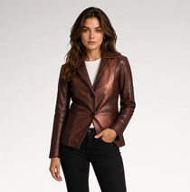 A woman modeling a metallic bronze-brown leather blazer over a white t-shirt and black jeans, photographed against a seamless light gray studio background.
