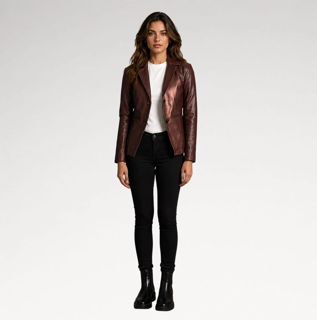 A woman stands against a light gray studio background wearing a metallic dark brown leather jacket over a white top, black skinny pants, and black ankle boots.