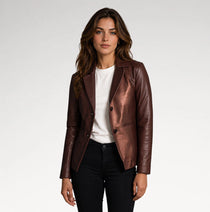 A woman modeling a metallic bronze-brown leather blazer over a white crewneck t-shirt and black jeans, photographed against a seamless light gray studio background.