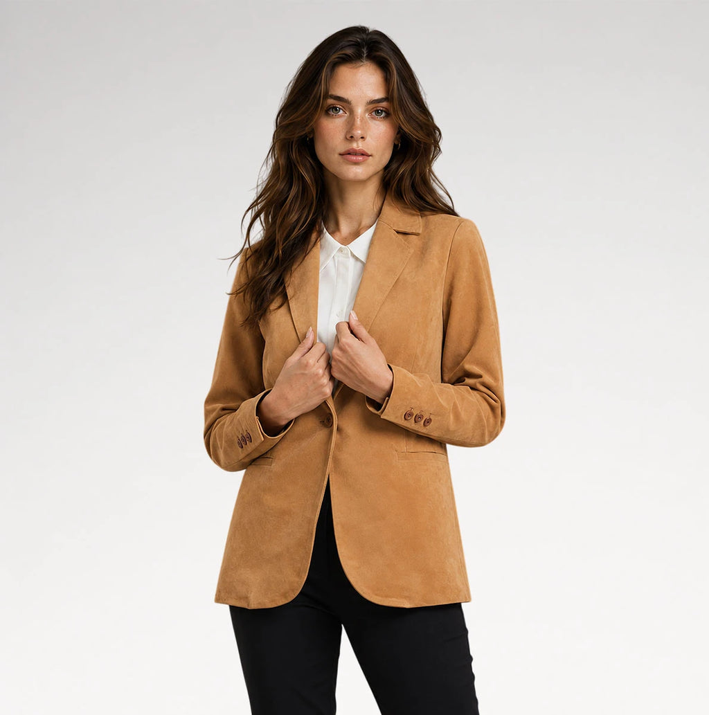 A woman modeling a camel brown suede blazer over a white collared shirt and black trousers, photographed against a clean light gray studio background.