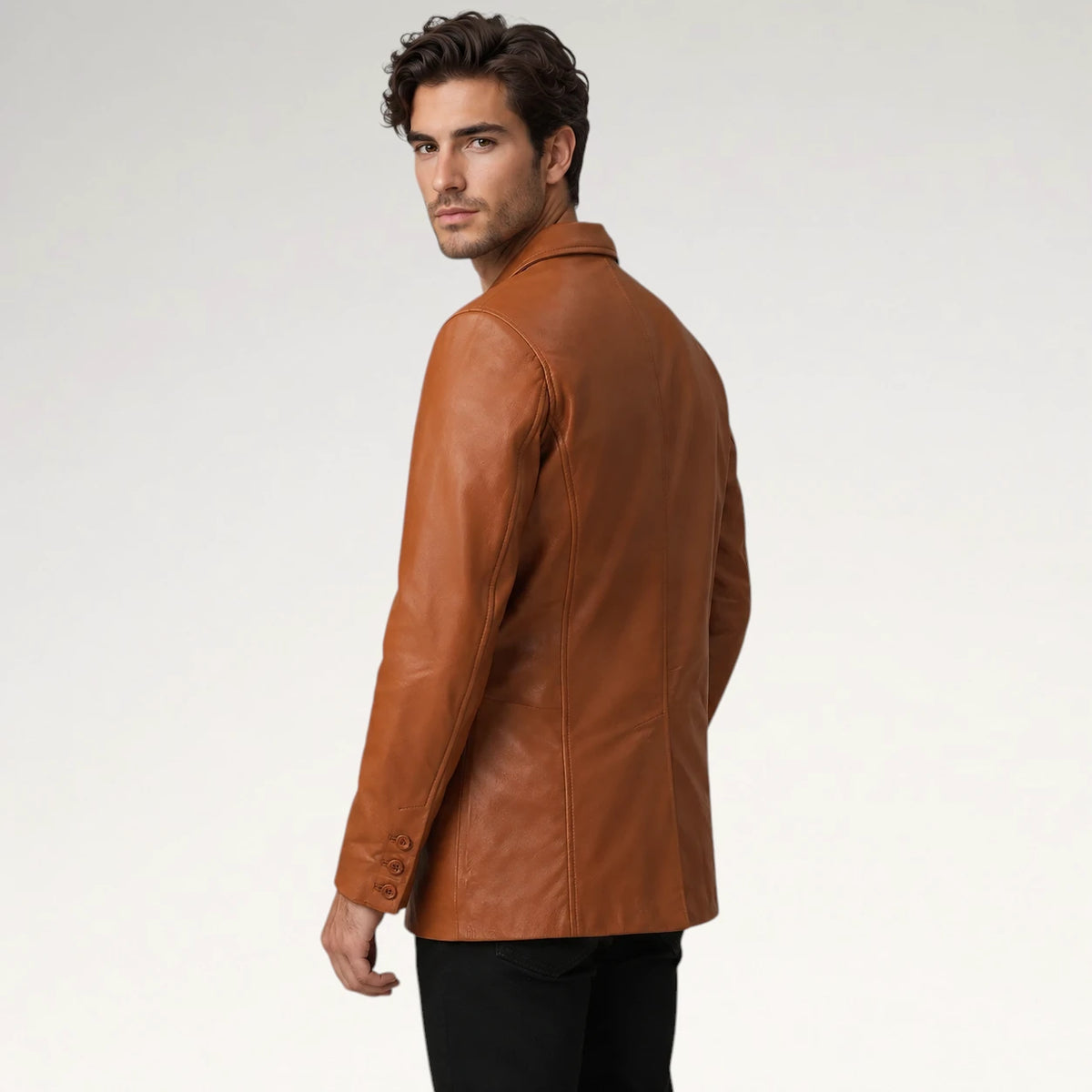 A man wearing a tan leather blazer, shown from a three-quarters back view against a light gray studio background.