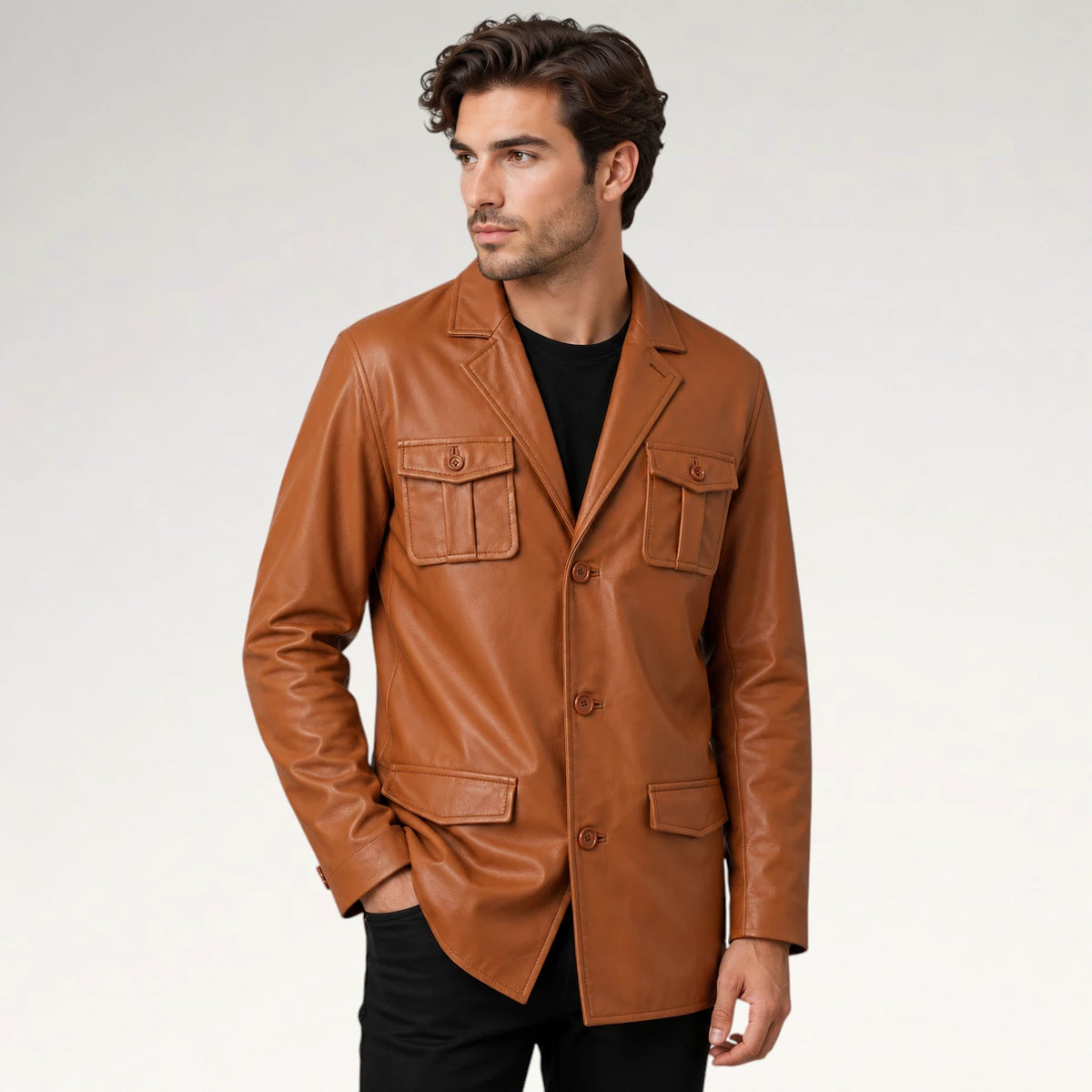 A man wearing a tan leather blazer with flap chest pockets, a button front, and angled front pockets, styled over a black t-shirt and black pants, photographed against a light gray studio background.