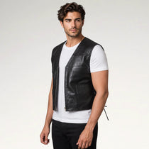 A man wearing a black leather vest over a white t-shirt and black pants, standing against a light gray studio background.