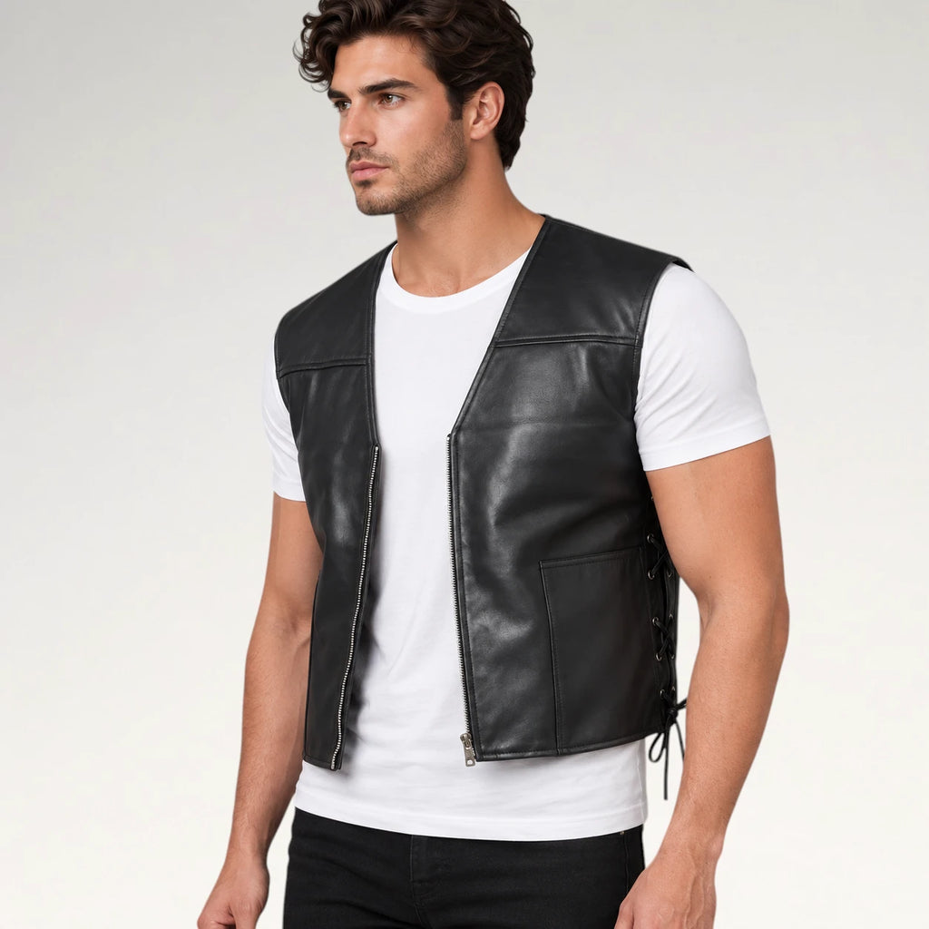 A man wearing a black leather motorcycle vest over a white t-shirt and black pants, photographed against a light gray studio background.