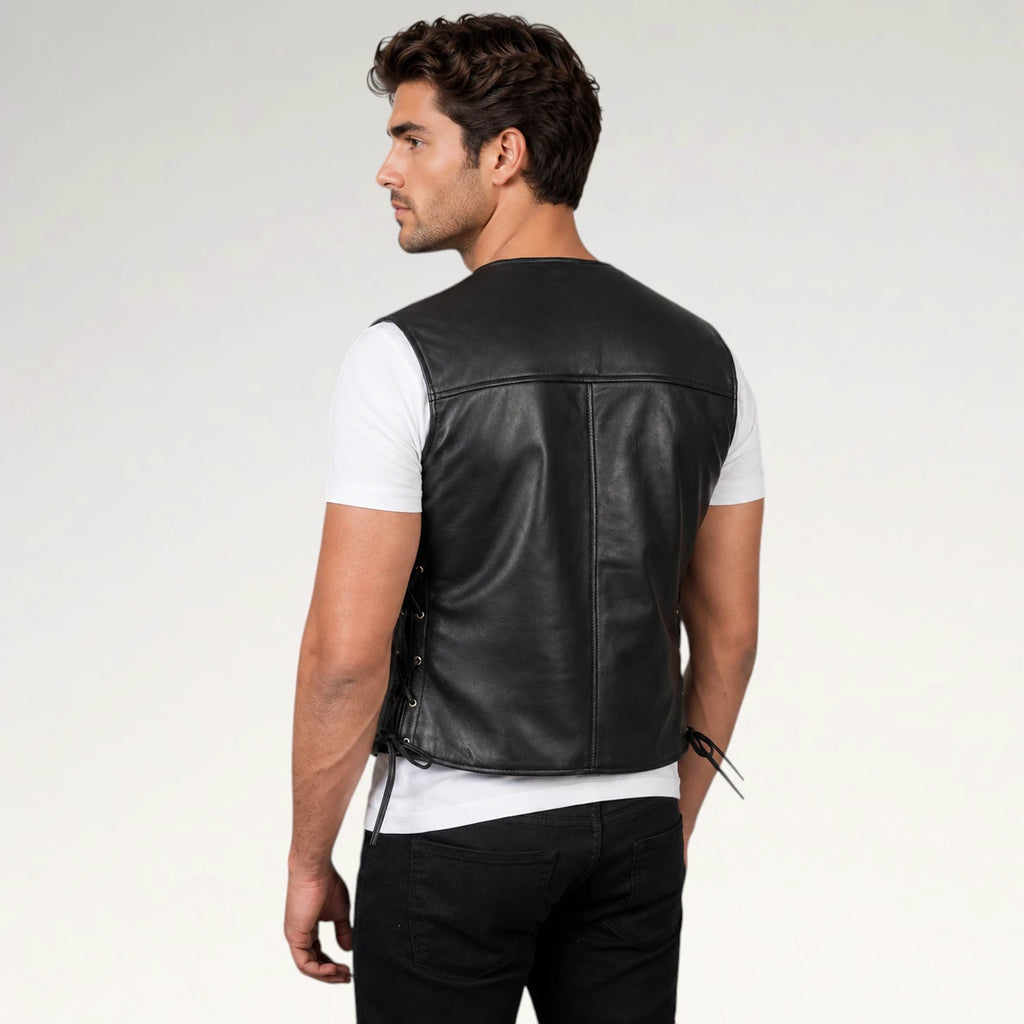 A man shown from the back wearing a black leather motorcycle vest over a white t-shirt and black pants, photographed against a light gray studio background.