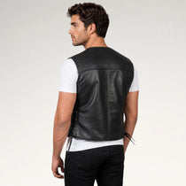 A man shown from the back wearing a black leather motorcycle vest over a white t-shirt and black pants, photographed against a light gray studio background.