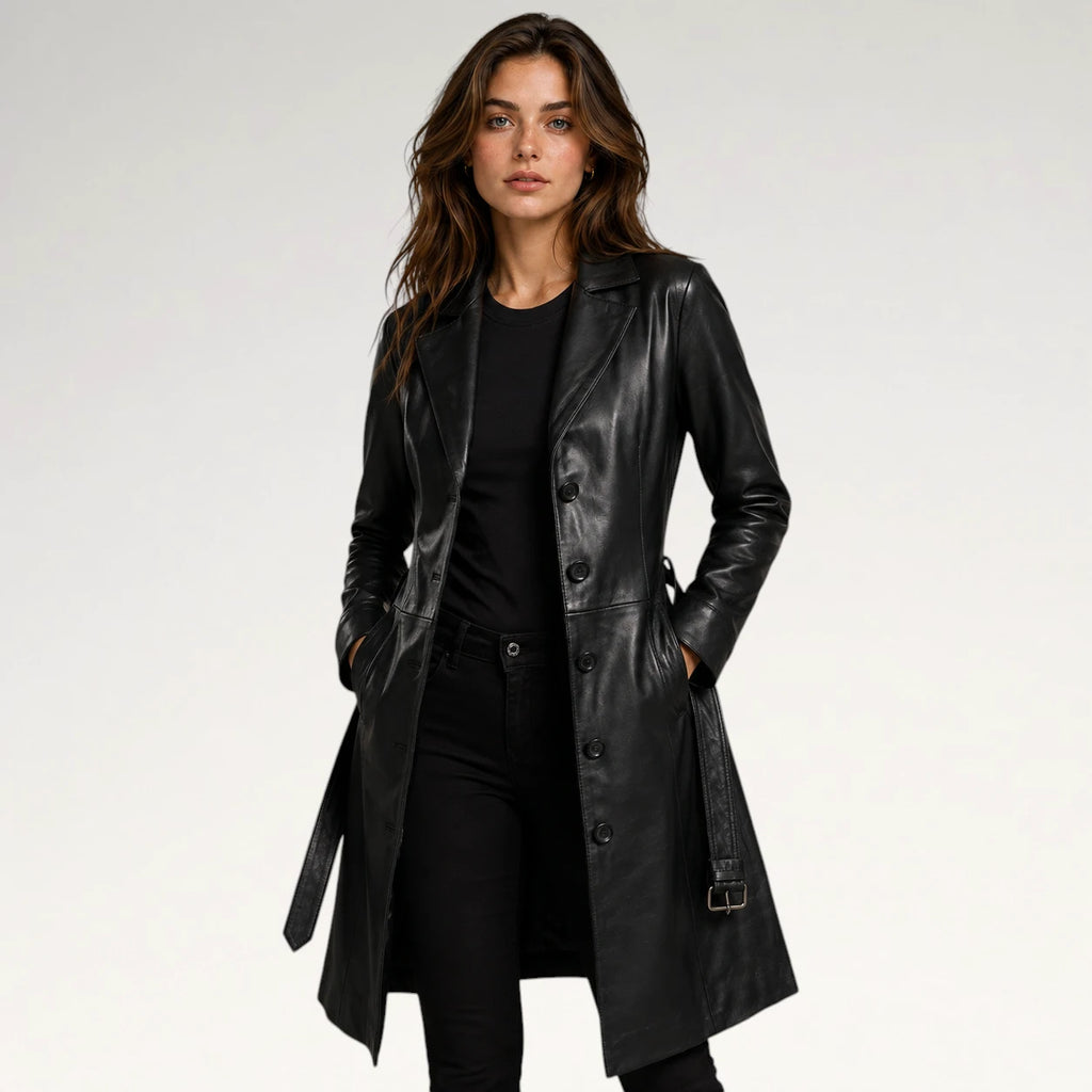 A woman modeling a black leather trench coat over a black outfit, photographed against a clean light gray studio background.