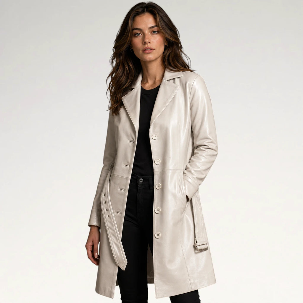 A woman modeling a light beige faux-leather double-breasted coat over a black top and black pants, photographed against a clean white studio background.