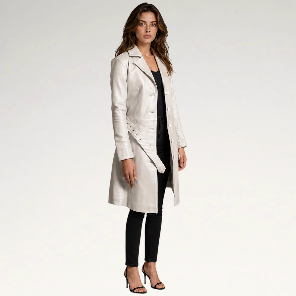 A woman modeling a long, light-colored leather coat over a black outfit, standing against a plain light gray studio background.