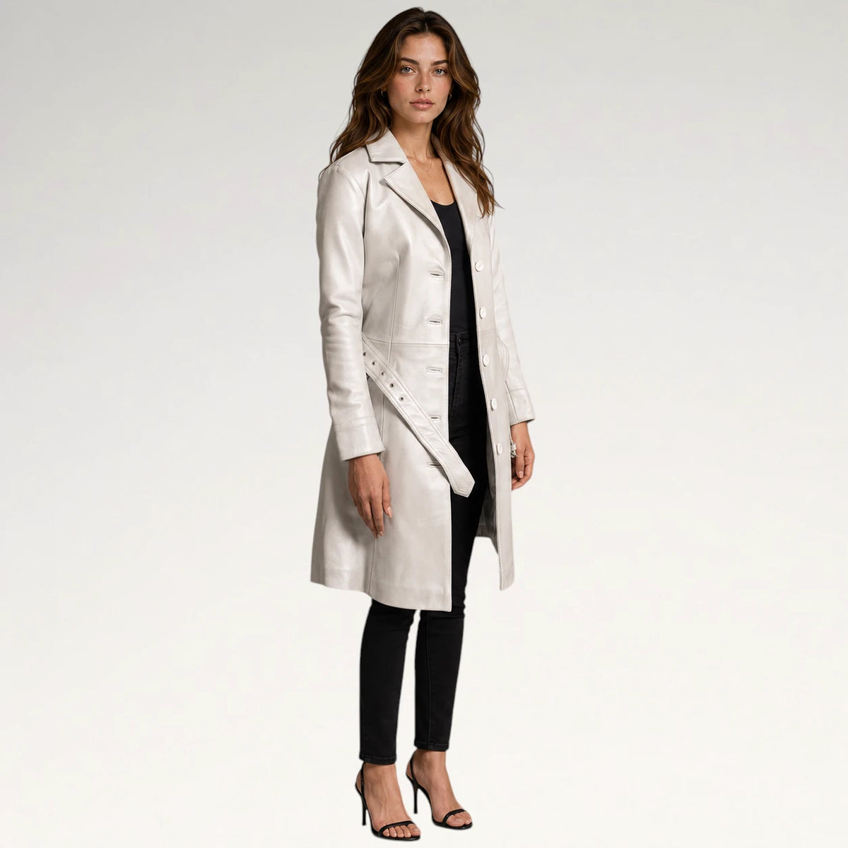 A woman modeling a long, light-colored leather coat over a black outfit, standing against a plain light gray studio background.