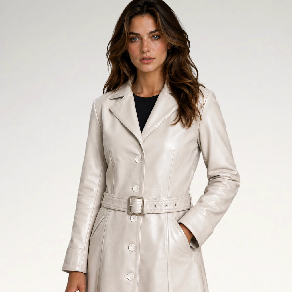 A woman modeling a light beige faux-leather trench coat with a matching belt and silver buckle, worn over a black top, against a plain light gray background.